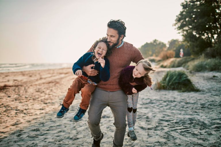 Man op het strand tilt zijn twee kinderen op, een moment van balans tussen werk en privé, ondersteund door recruitment outsourcing.